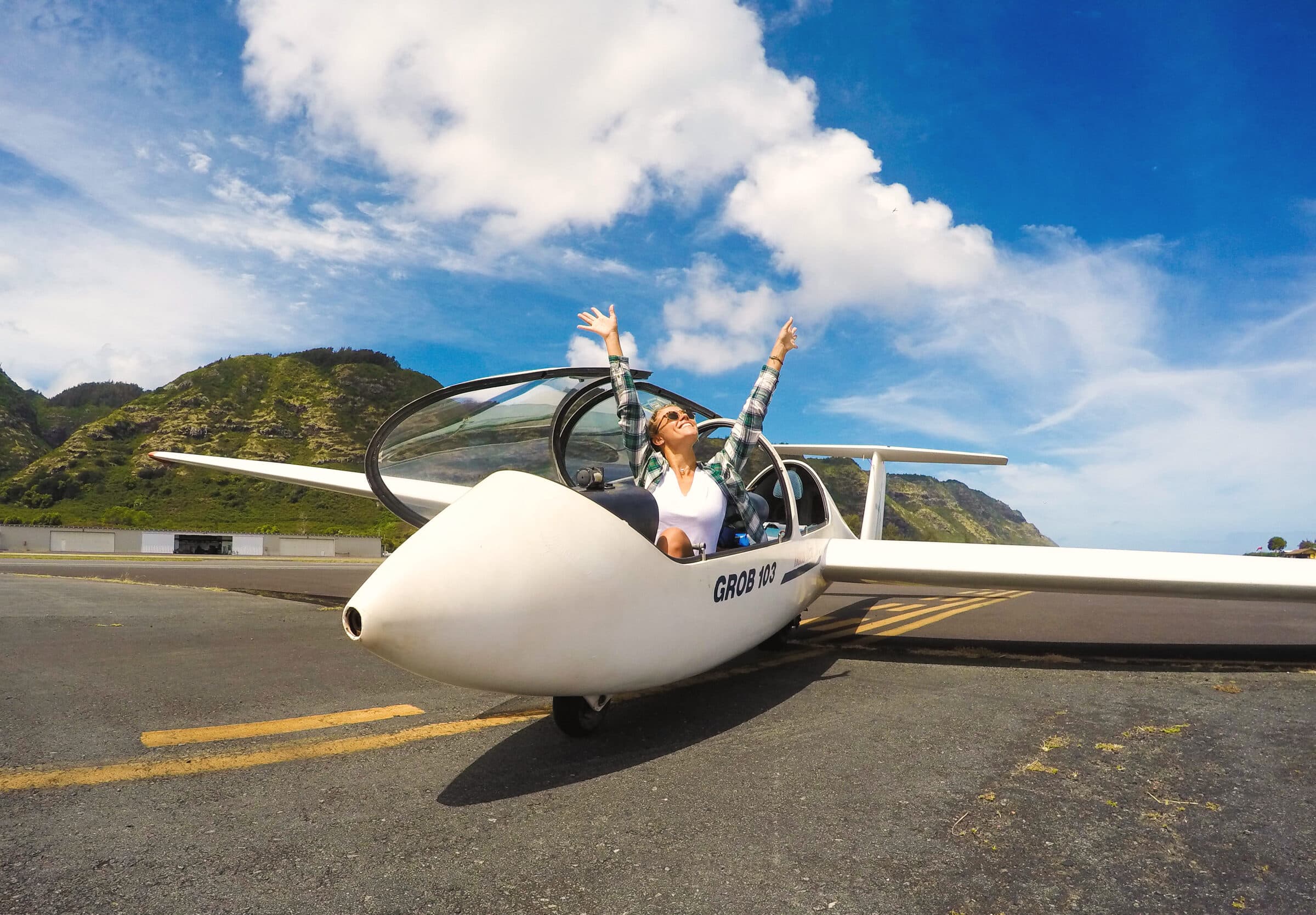 Delighted passenger throwing their arms up beside a glider on the Mokulēia runway
