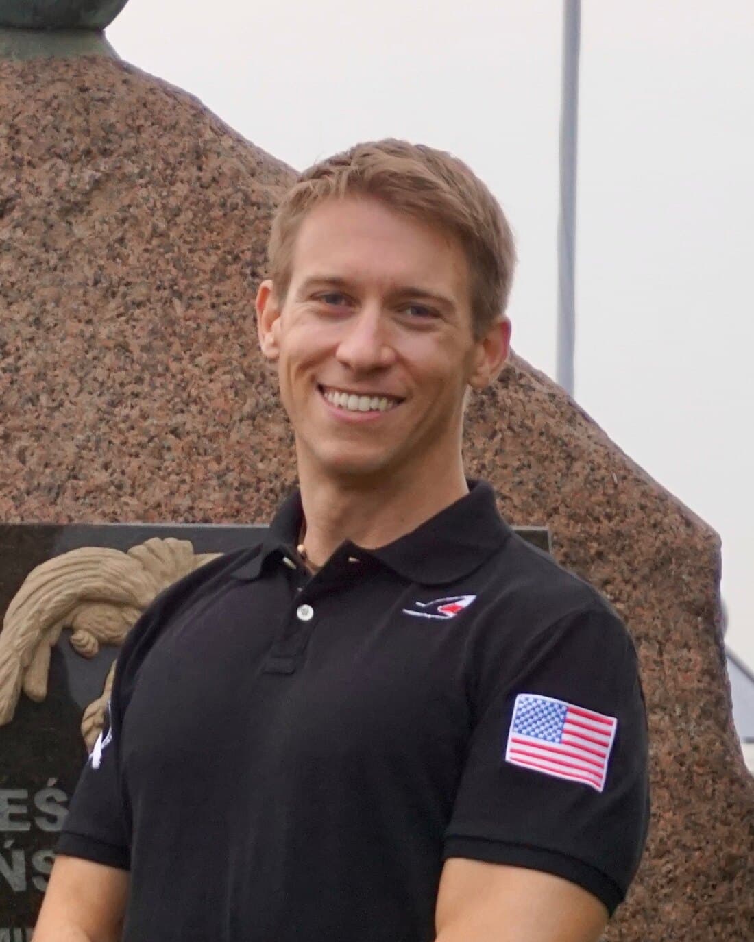 James Alaggio smiling in front of a stone soaring memorial at an airfield