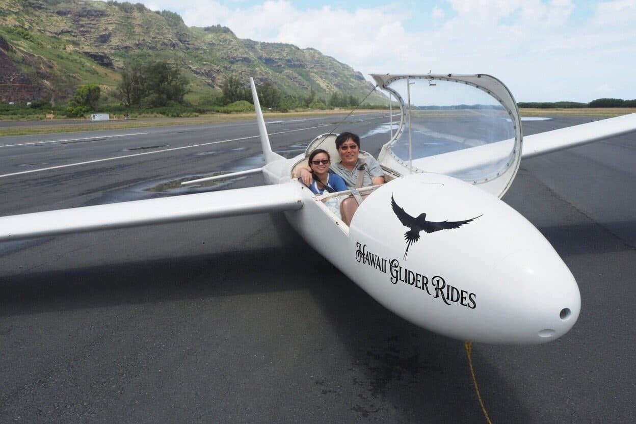 Two passengers smiling beside a glider at Dillingham Airfield on Oahu