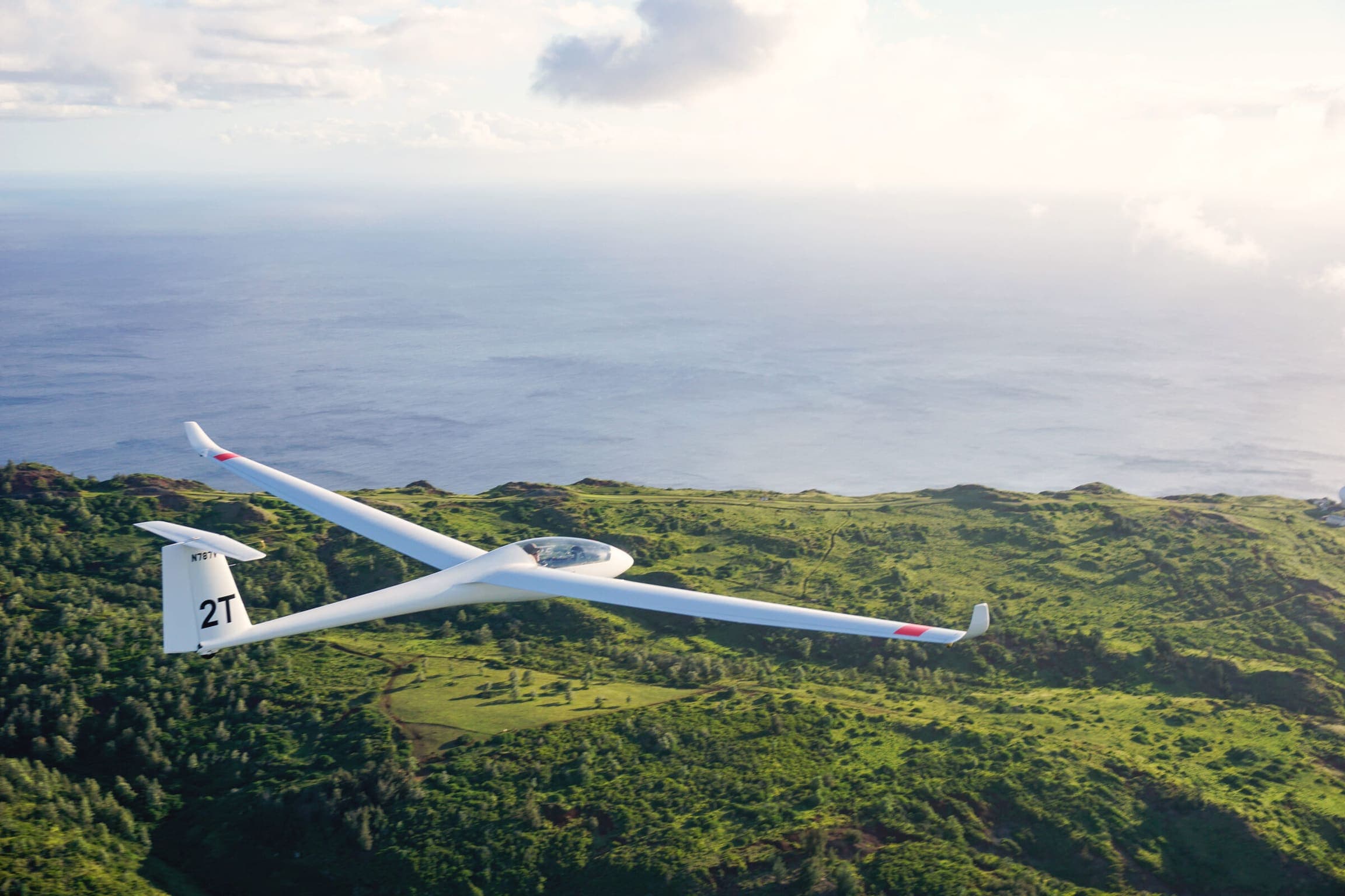 White glider over the green ridgelines of Oahu with the ocean beyond