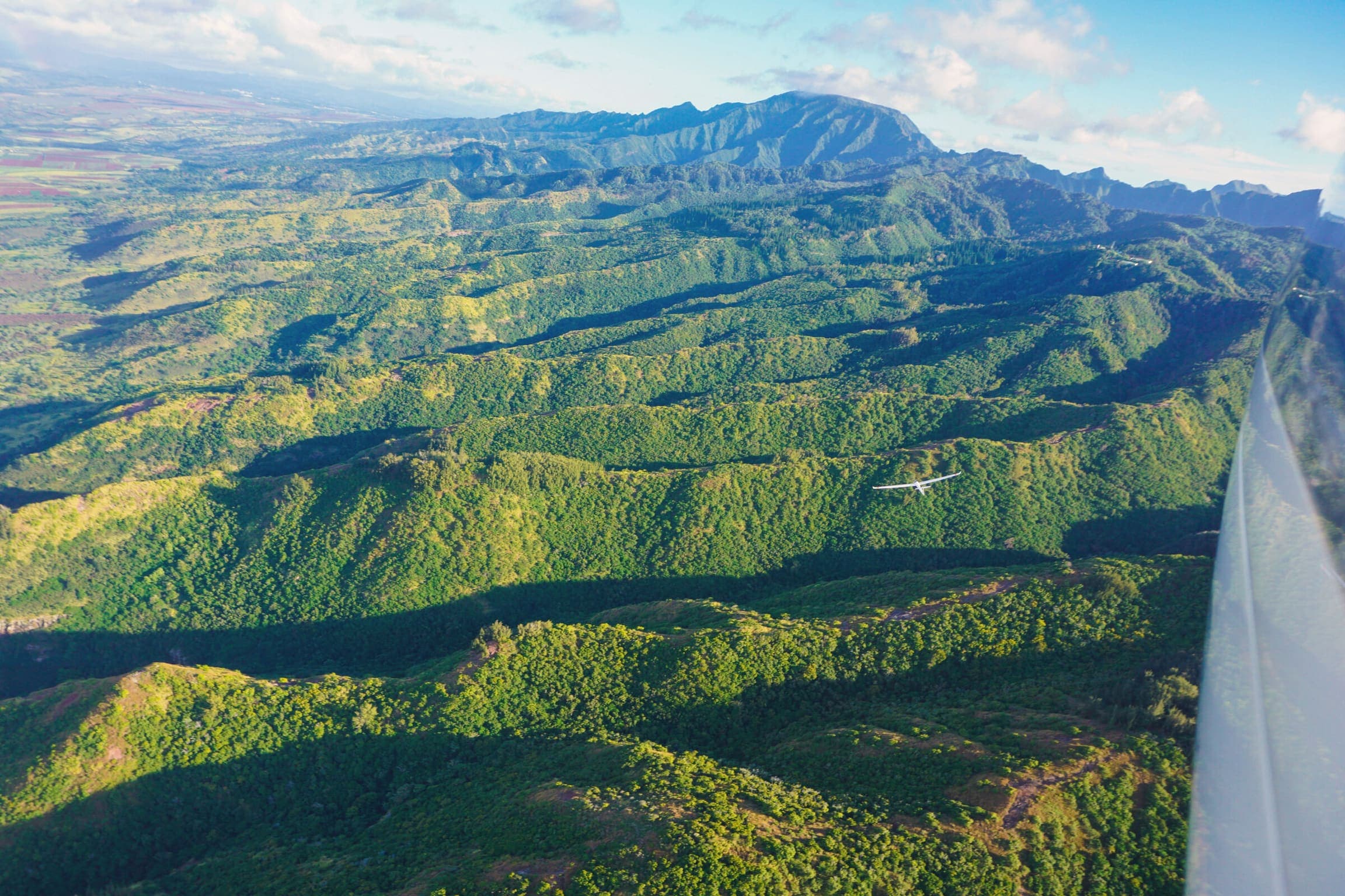 Glider flying above the green Waiʻanae mountains on Oahu's North Shore